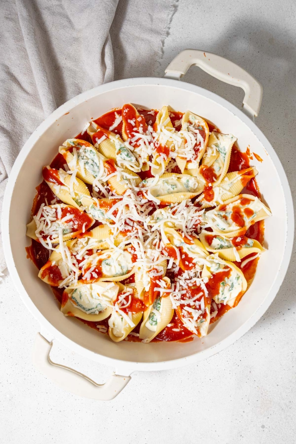 An unbaked pot of cottage cheese stuffed shells in marinara sauce topped with shredded mozzarella cheese.