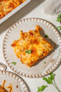 A square slice of million dollar spaghetti on a plate garnished with fresh parsley.