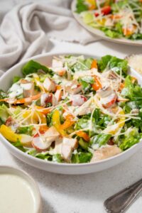 A bowl of healthy chicken Caesar salad with shredded parmesan and dressing.