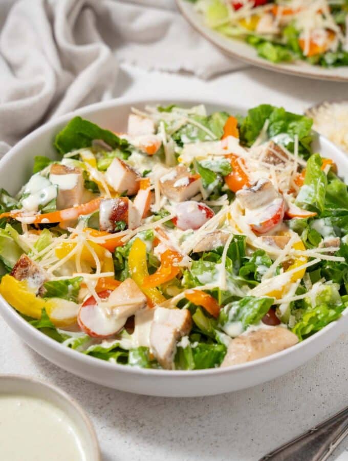 A bowl of healthy chicken Caesar salad with shredded parmesan and dressing.