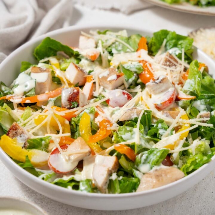 A bowl of healthy chicken Caesar salad with shredded parmesan and dressing.