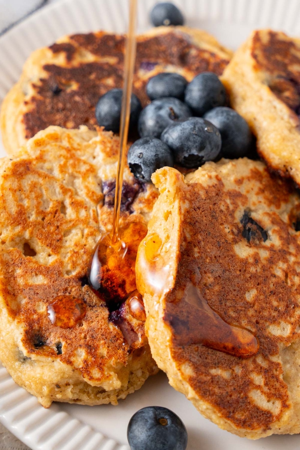 Maple syrup being drizzled on cottage cheese banana blueberry pancakes.