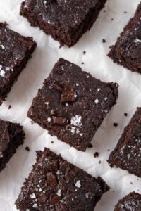Neatly arranged cottage cheese brownies topped with flaky sea salt on a parchment paper.