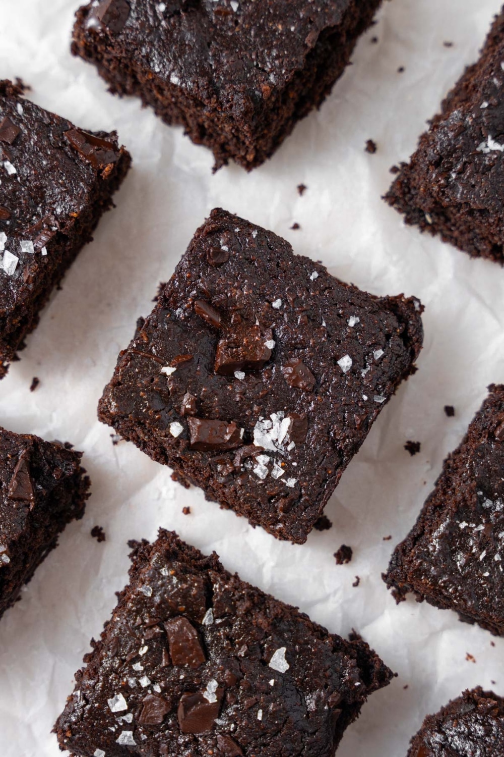 Neatly arranged cottage cheese brownies topped with flaky sea salt on a parchment paper.