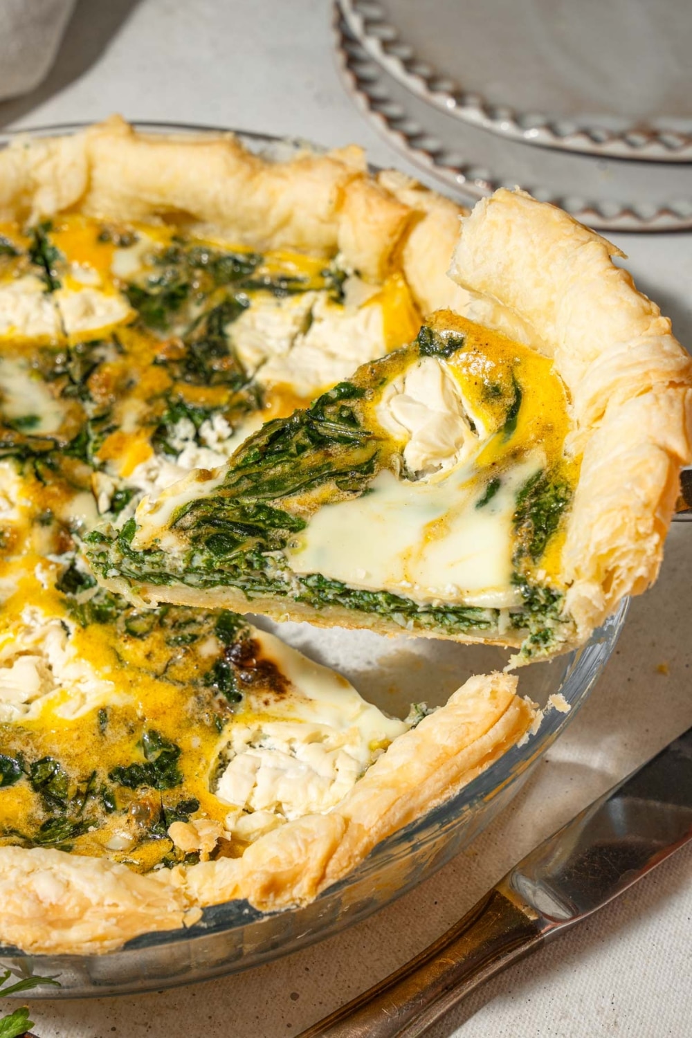 A slice of spinach cottage cheese quiche being lifted from a pie pan.