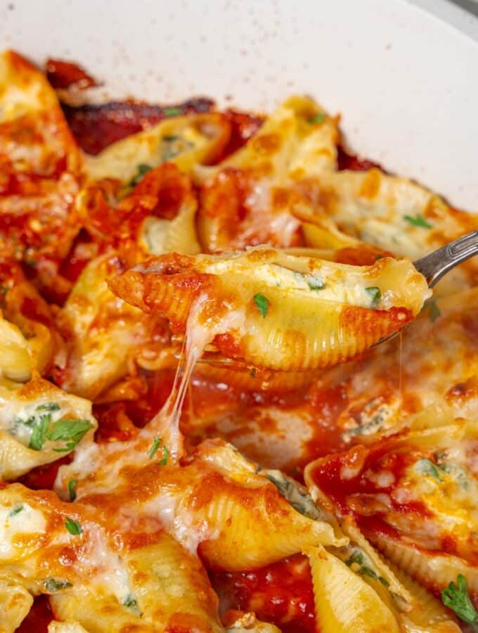 Lifting a stuffed pasta shell from a pan of cottage cheese stuffed pasta shells in marinara sauce.
