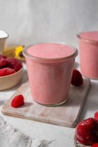 Strawberry cottage cheese smoothie in a glass set on a wooden board. Another smoothie is in the back.