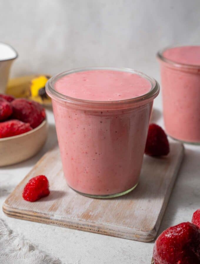 Strawberry cottage cheese smoothie in a glass set on a wooden board. Another smoothie is in the back.
