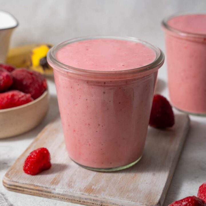 Strawberry cottage cheese smoothie in a glass set on a wooden board. Another smoothie is in the back.