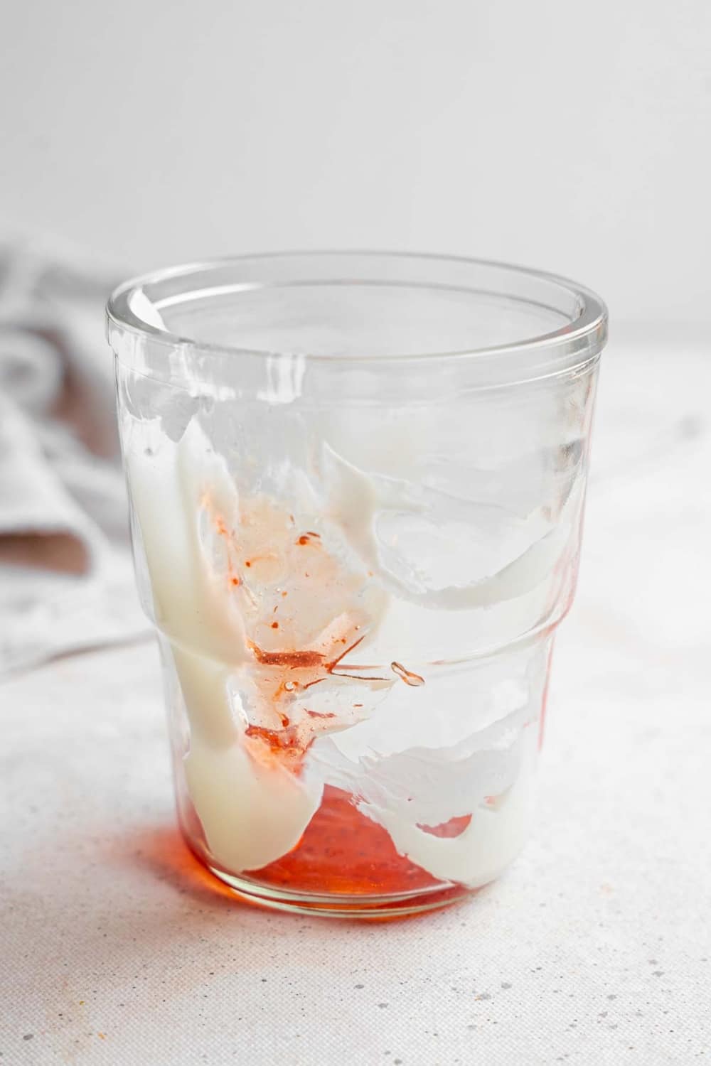 An empty glass decorated with coconut cream and jam at the base. The glass is on a marble counter with a white cloth napkin in the background.